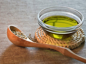 Hemp oil and seeds are displayed next to each other in a bowl and spoon respectively